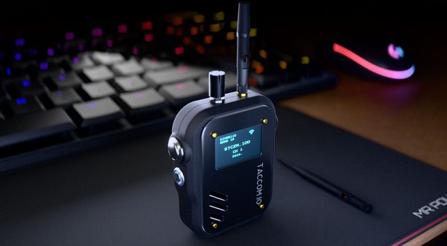 The TACCOM handheld radio resting on a desk beside a backlit keyboard